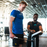 man op weegschaal krijgt uitleg van coach