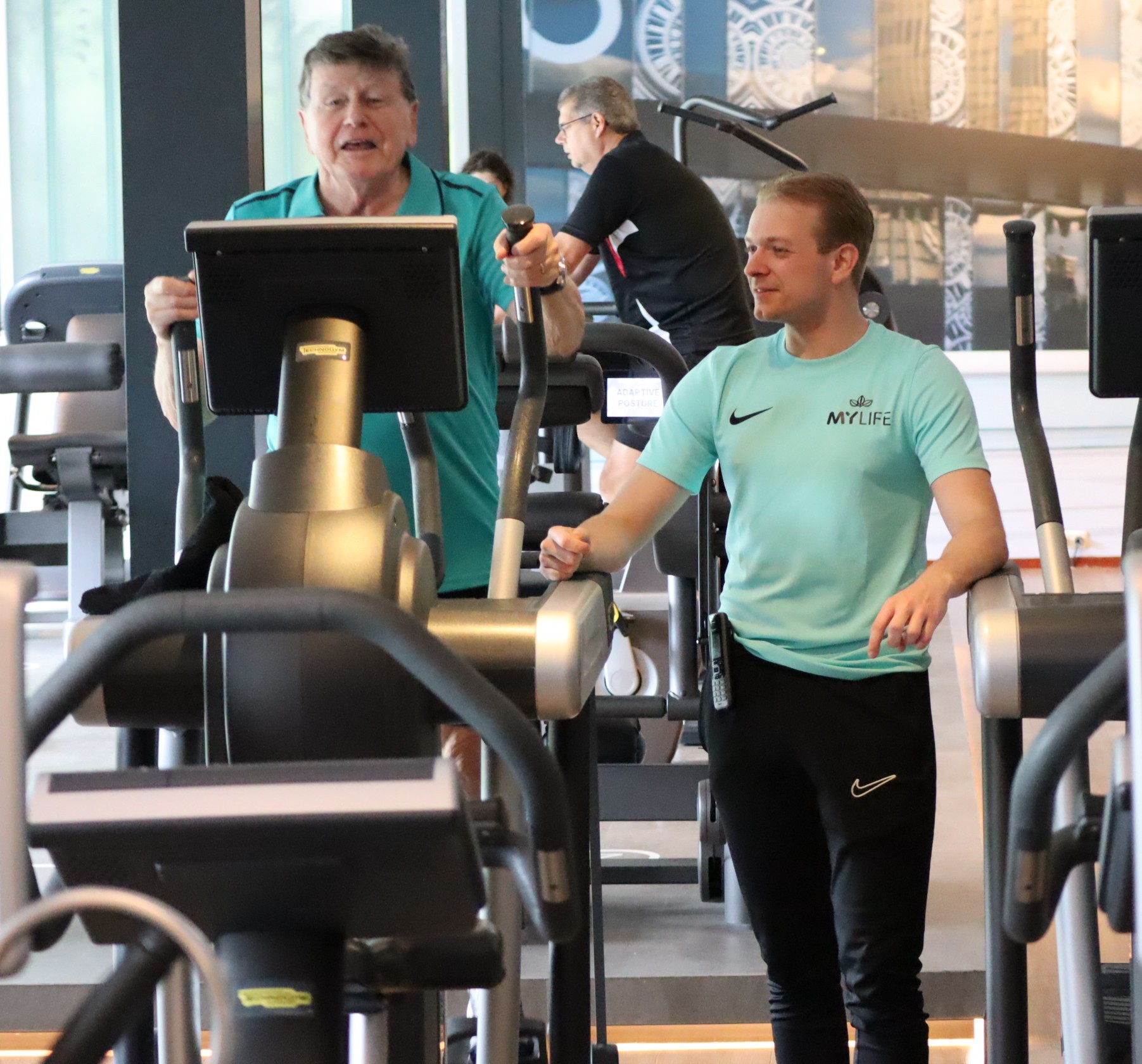 man op fitnessapparaat krijgt begeleiding van instructeur